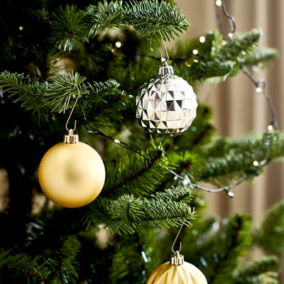 Dekorative Weihnachtsornamente: gelbe runde Kugel und geometrisches Silberornament, das an Kiefernästen hängt.