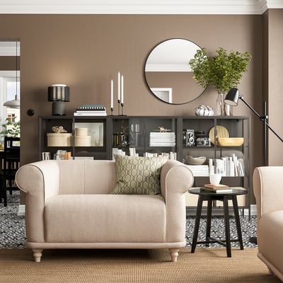 Modernes Wohnzimmer mit VISKAFORS-Sessel, beigefarbenem, rundem Couchtisch, schwarzem Regal, Stehleuchte und beigem Teppich.
