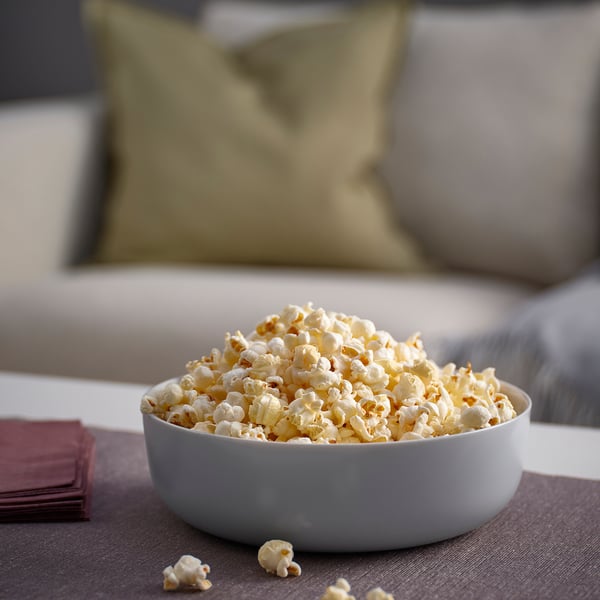 Schüssel Popcorn auf der Couch. Weiße VITBLECKA Glasschale, groß, rund, schlichtes Design. Die Schüssel fasst eine beträchtliche Menge Popcorn, in der Nähe von burgunderroten Servietten.