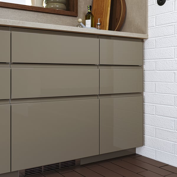 Moderne Küche mit schlanken, dunkelgrau-braunen VOXTORP-Schubladenfronten mit glänzender Oberfläche, die von einer weißen Backsteinwand abgesetzt ist.