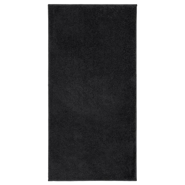 A black rectangular BACKMÅRA bath mat made of recycled polyester, featuring a soft pile and latex backing.