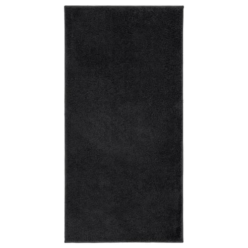 A black rectangular BACKMÅRA bath mat made of recycled polyester, featuring a soft pile and latex backing.