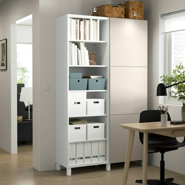White BESTÅ storage with adjustable shelves, tall and sleek between door and desk, holding boxes, books, and decor.