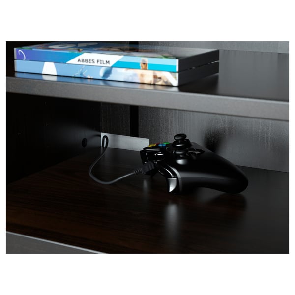 Black gaming controller on dark wood tv stand with shelf for movie cases.