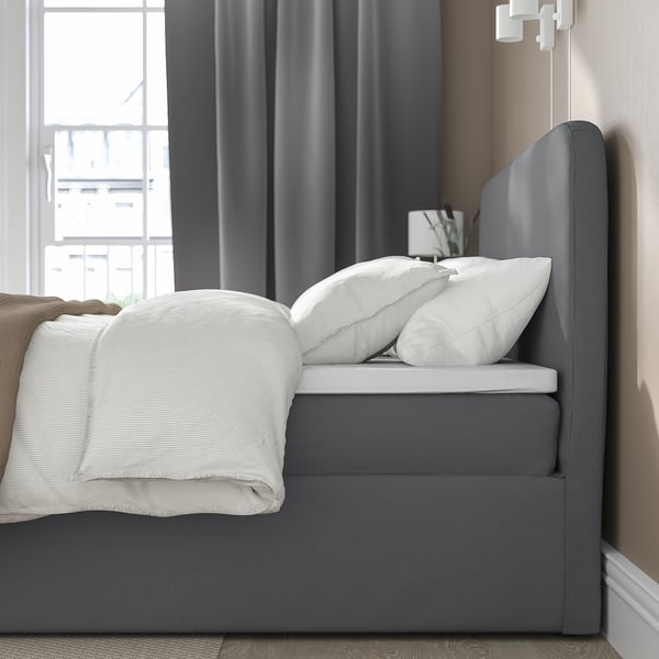 Neatly made bed with white pillows, grey headboard, and storage area.