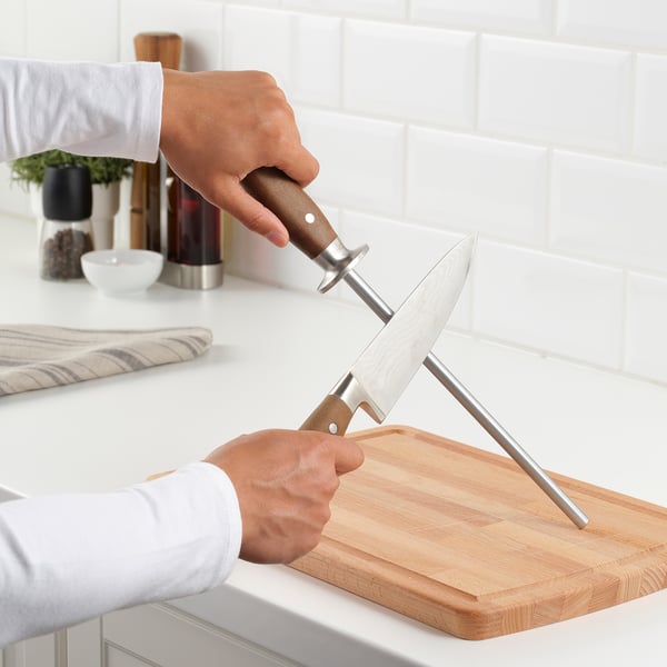 Person sharpens knife on BRILJERA sharpener, ensuring blade remains sharp and safer to use. Knife stands on cutting board.