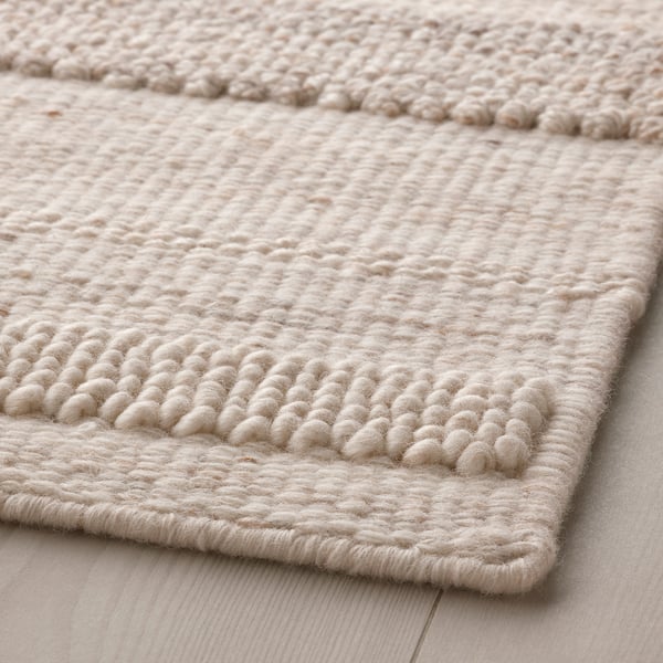 Handwoven beige rug on wooden floor. Textured wool surface, finely crafted for durability.