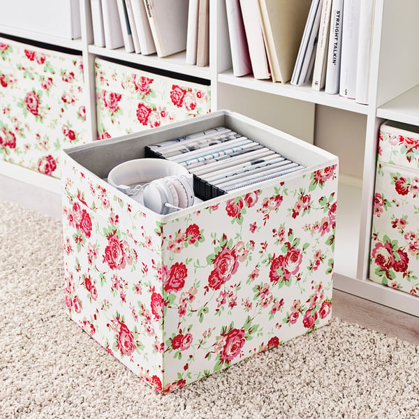 Floral storage box on shelf with headphones and cables, part of kallax unit.