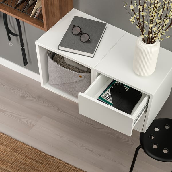 White EKET storage unit with two open compartments, one containing a grey felt bin and the other a black drawer with visible books and gloves.