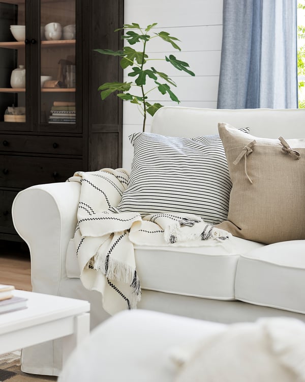 Modern living room with white EKTORP sofa, striped pillows, fringe throw, and potted plant.