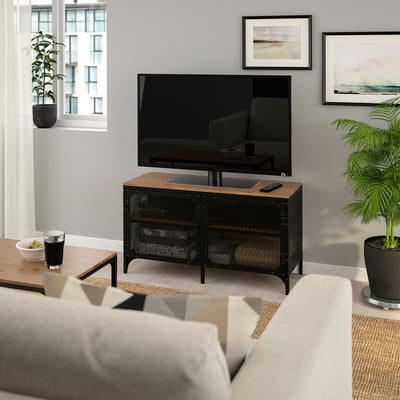 FJÄLLBO tv stand with mesh doors under flat screen, in rustic living room with couch & plants.