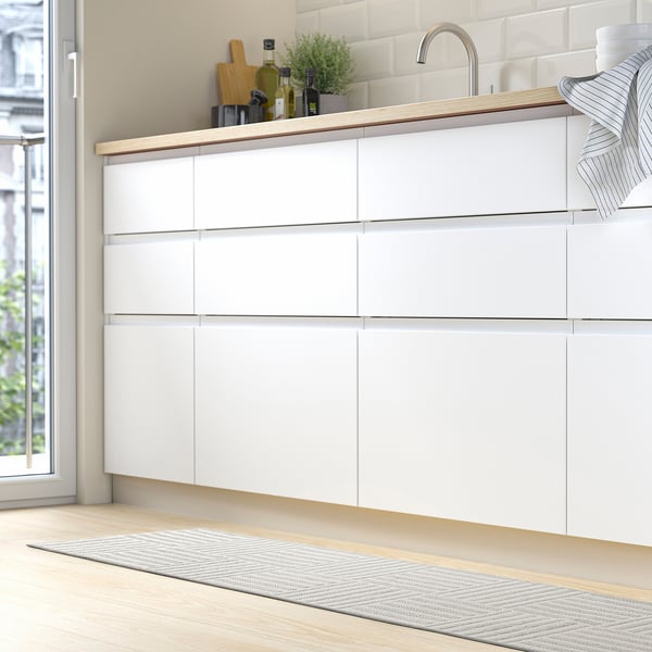 Modern kitchen with white cabinets and striped mat, small potted plant, kitchen knives, and oil on counter.
