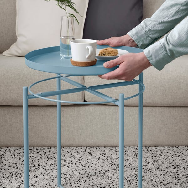 Person holding a blue tray table with a coffee cup and treat, sitting on a beige couch.