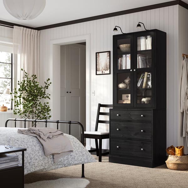 Modern bedroom with dark HAVSTA drawers & glass cabinet, white walls, metal bed, plant, chair, rug.