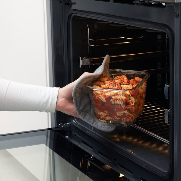 Hand places glass dish with pasta into black oven, showcasing its oven-safe use and convenience.
