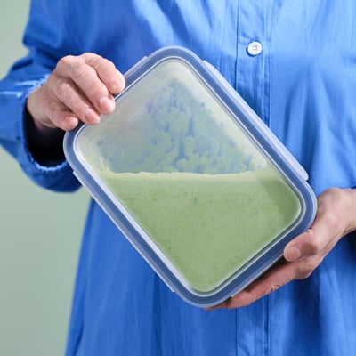 Person holding a transparent plastic container with a green smoothie and a locking lid.