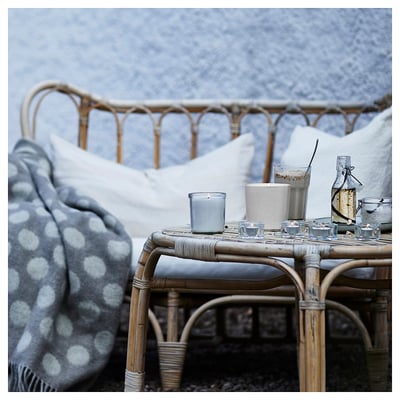 Rattan furniture set with blue polka dot blanket, pillows, blue candle, glass jars, and bottle on wicker coffee table. Calm scene with snowy backdrop.