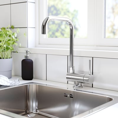 Modern kitchen sink with chrome tap, black soap dispenser, and a green plant.