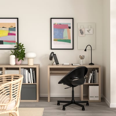 Home office with wooden desk, black swivel chair, and bookshelves, adorned with colourful art and neat decor.