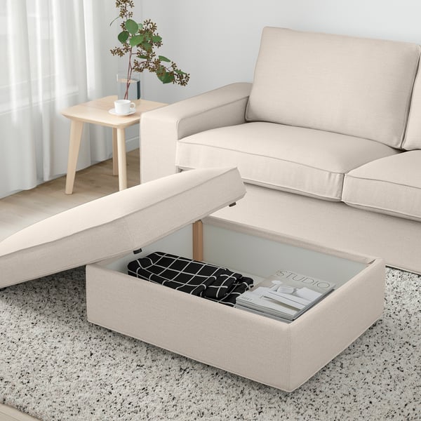 L-sofa with lift-top storage and magazines, side table with plant and coffee by window.