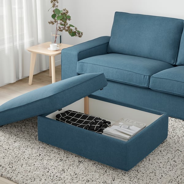 KIVIK blue footstool with storage, holding magazines and blanket. Next to blue sofa and side table.