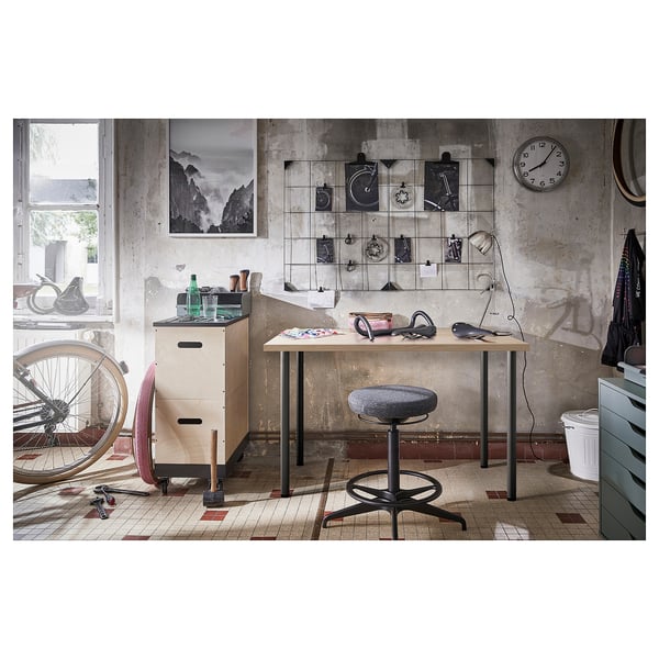 Industrial-style workspace with wooden desk, grey stool, metal cabinets, and wall art.