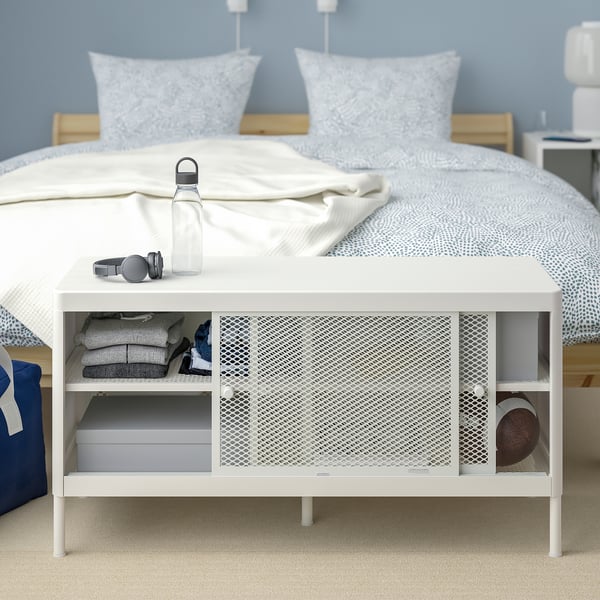 White MACKAPÄR bench in bedroom with shelves and sliding mesh doors for hidden storage.