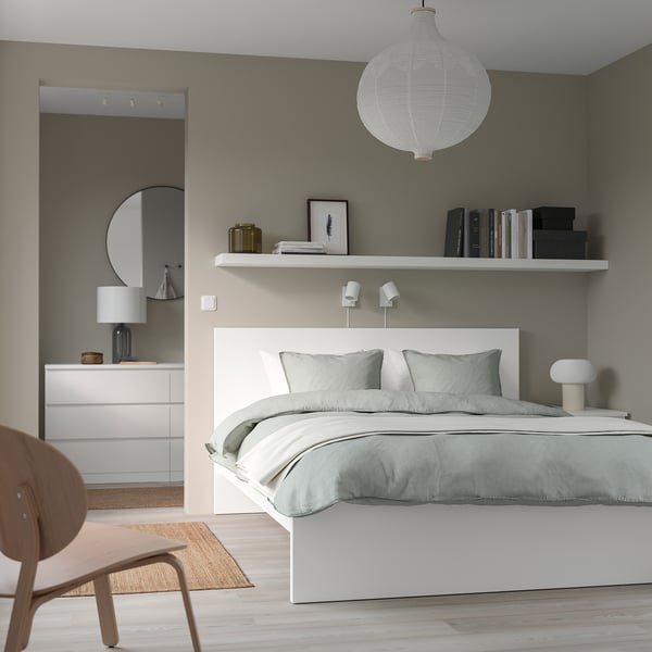 Modern minimal bedroom: white MALM bed, pendant lamp, grey bedding, wall shelf with books, dresser, mirror, lamp, wooden chair.