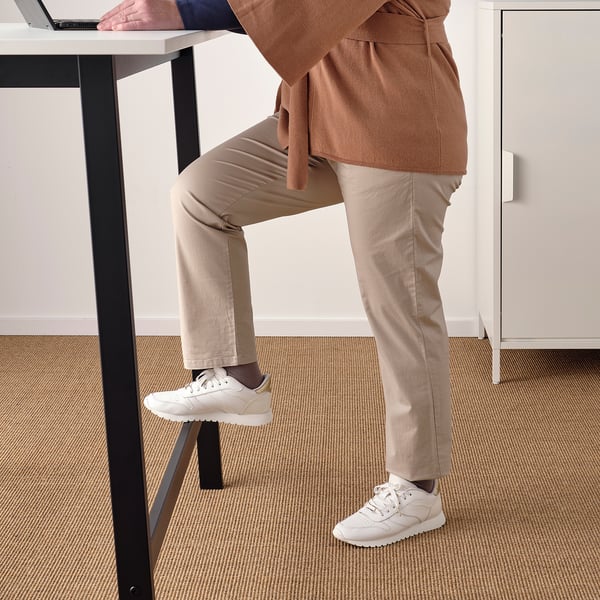 Person using standing desk with laptop and footrest for comfort.