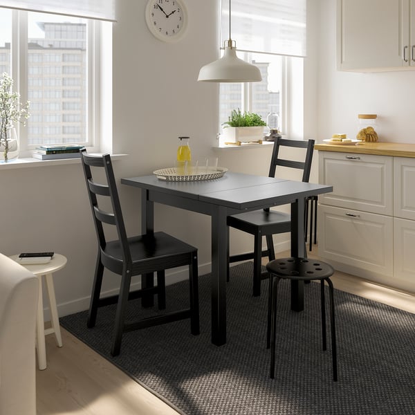 Small black NORDVIKEN dining set in bright kitchen. Includes extendable table and chairs, positioned near white cabinets.
