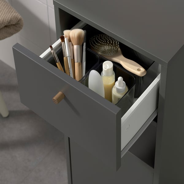 Open grey bathroom cabinet with drawer. Stores toiletries, brushes, and bottles.