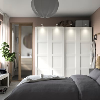 Modern bedroom white PAX wardrobe with soft lighting, slate bedding, and a potted plant.