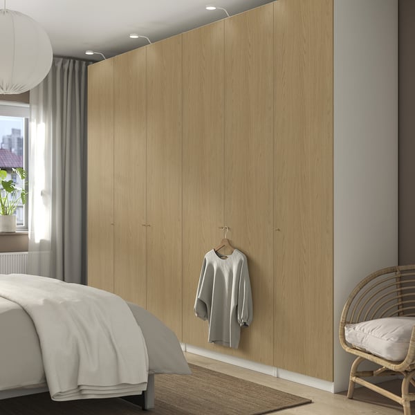 Modern beige wooden PAX wardrobe spans entire wall, taller than bed, housing grey sweater.