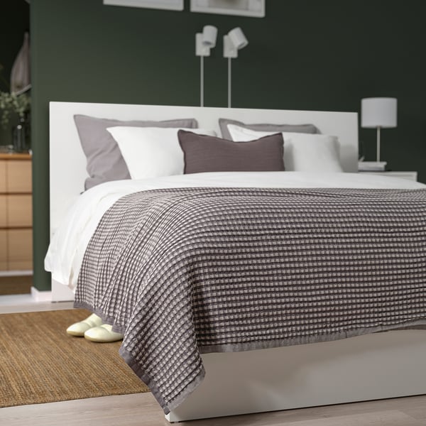 Greyscale PELARTUJA bedspread on bed with headboard, pillows, slippers on rug, dark green walls, minimal decor.