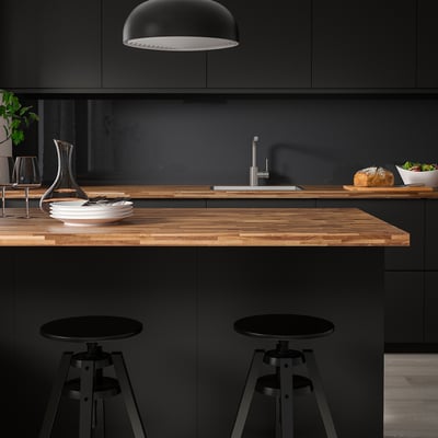 Modern kitchen with dark green cabinets, wooden island countertop, two black bar stools, plates, wine glasses, and a carafe.