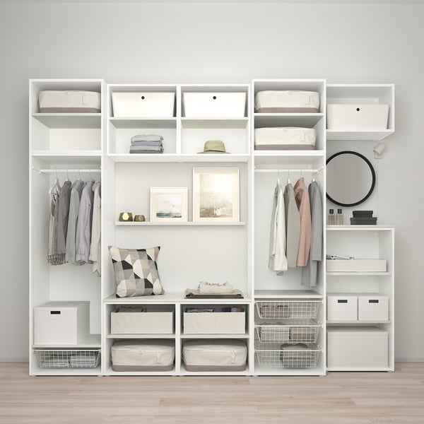 Modern white wardrobe with shelves, drawers, and hanging space for clothes. Includes decorative items like pillows, hat, and art frames.