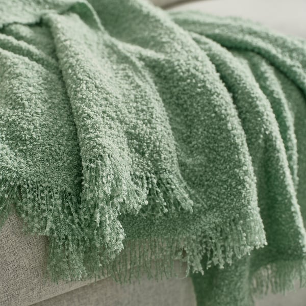 Pile of soft, green, textured throws made from recycled polyester, draped neatly.