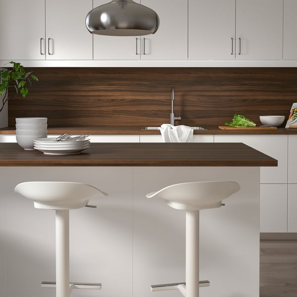 Modern kitchen with white cabinets, wooden countertop, white stools, metal pendant light, and stacked dishes.