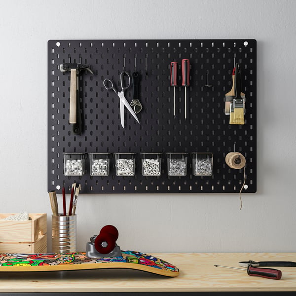 SKÅDIS black pegboard organises tools above desk, holding hammers, scissors, screwdrivers, and containers.