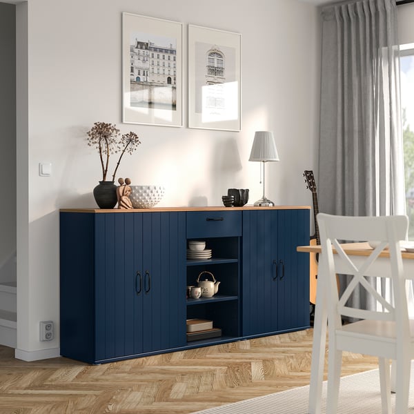 Modern dining room with SKRUVBY blue sideboard, white chair, wooden floor, grey curtains, photos, and lamp.