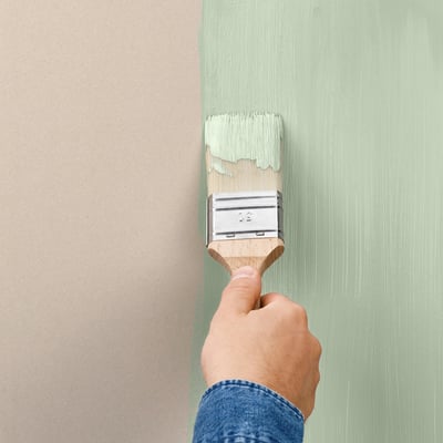 Hand painting wall with light green paint using a brush.