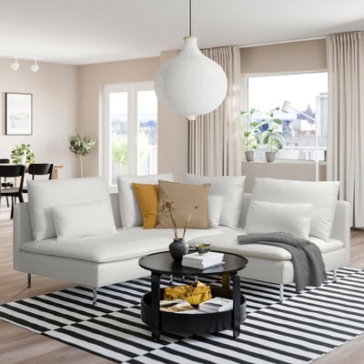 Modern living room with SÖDERHAMN sofa, wooden floor, striped rug, coffee table with books, and large window with beige curtains.