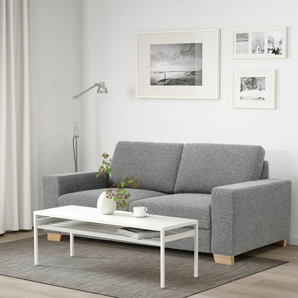 A modern living room with a grey sofa, white table, and lamp. Wall art decorates light-colored walls.