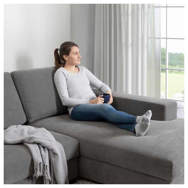 Person on SÖRVALLEN sofa, holding mug, looking out window.