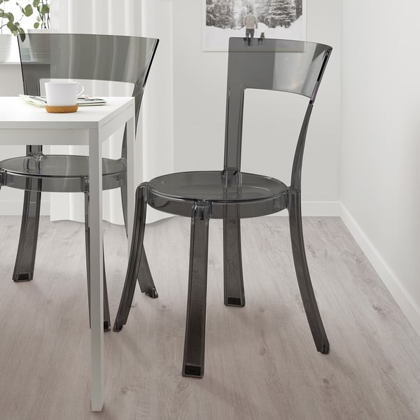 Two modern, transparent, stackable chairs near a dining table with cups placed on it.