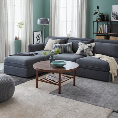 Cosy living room with large grey STOENSE rug, sectional sofa, wooden coffee table, and green walls.