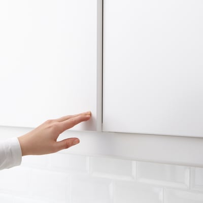 A hand pushing a cabinet door to open it, demonstrating a push-opener mechanism.