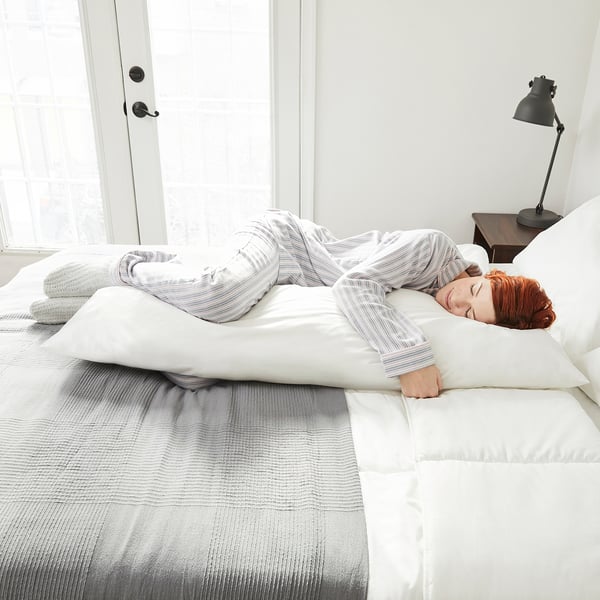 Person resting on side with long body pillow on bed.