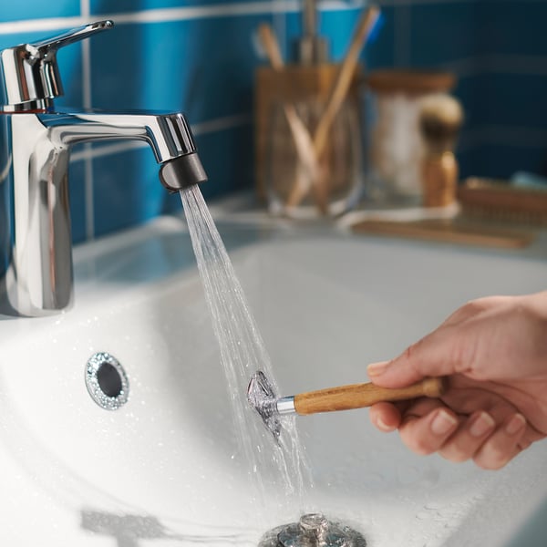 A person washing a toothbrush under a modern silver tap with a chrome ÅBÄCKEN nozzle in a blue-tiled bathroom.