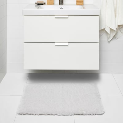 White ALMTJÄRN bath mat beneath sink, soft and textured, square with fringe, fits under vanity.